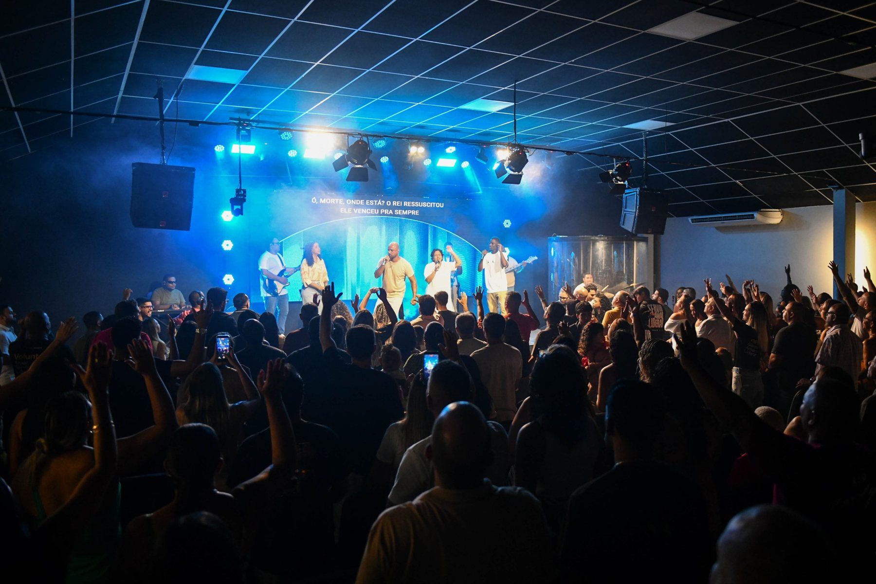 Culto da Igreja Incomum Guapimirim com louvor no palco e a igreja de mãos levantadas